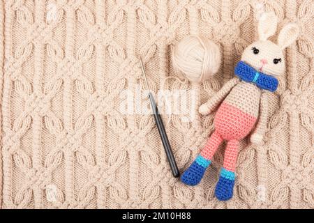 Knitted children's toy hare or rabbit with a ball of thread and a crochet hook on a knitted beige cloth. The symbol of 2023. Stock Photo