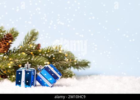 Three Christmas decorations in the form of blue gifts near the Christmas tree with twinkling golden lights on a blue background. Merry Christmas and N Stock Photo