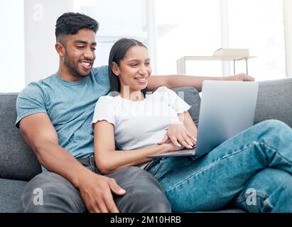Taking a movie break. a young couple sitting on the sofa in their new home and using a laptop. Stock Photo