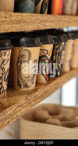 A vertical shot of row of compostable coffee cups with artistic prints on wooden shelves Stock Photo