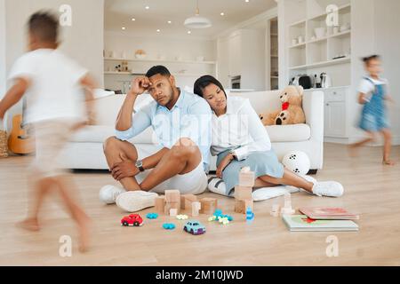 It aint all fun and games. a young couple looking stressed at home while their kids play around them. Stock Photo