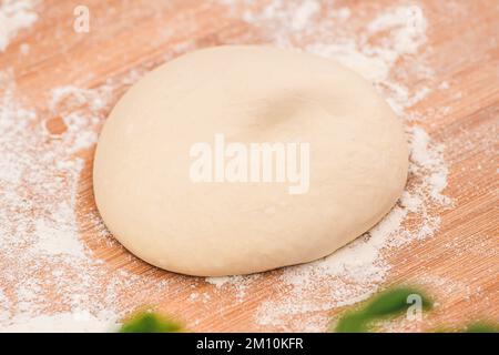 Preparing dough for pizza on a wooden board with white flour and ingredients around, close up, copy space Stock Photo