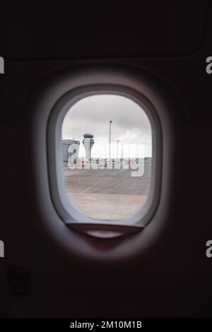 views from the plane overlooking the runway with its boarding bridge and control tower. It is a very gray day. Stock Photo