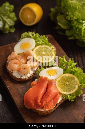 The toasts with boiled eggs, salad lettuce, lemon slime, shrimps and smoked salmon. Stock Photo