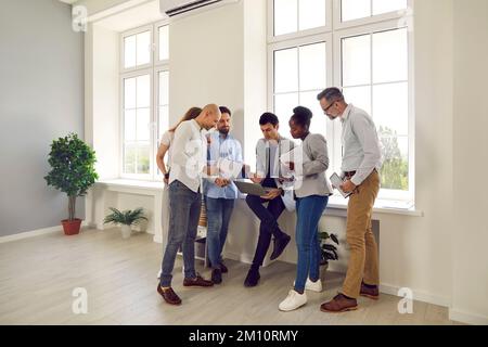 Diverse business team standing by office window and using laptop computer together Stock Photo