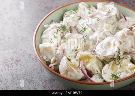 New potato salad with pickles, dill and red onion with sour cream dressing close-up in a plate on the table. Horizontal Stock Photo