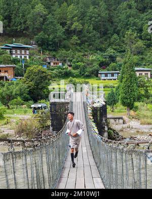 Young monk crosses suspension Bridge near Punakha Bhutan Stock Photo