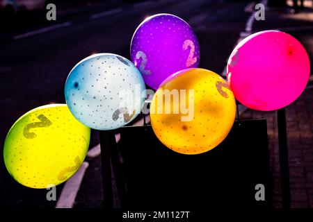 5 brightly coloured balloons in the street with a figure 2 printed on them.Back lit by the Sun makes a dramatic image Stock Photo