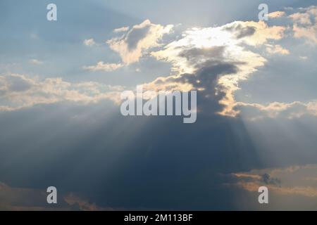 Streaks of the sun behind the clouds of blue sky Stock Photo