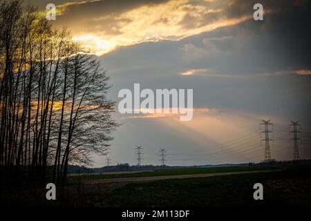 Sunset - rays breaking through the clouds. In the background, the power grid, electricity poles. Stock Photo