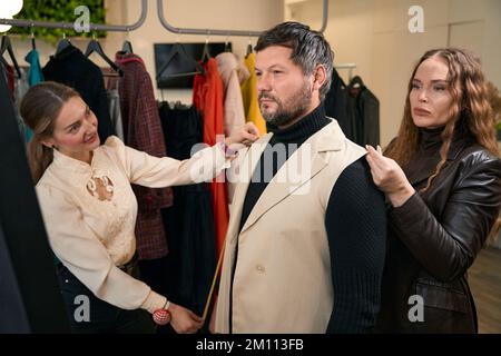 Dressmakers try on a semi-finished product for a middle-aged client Stock Photo