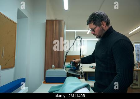 Young man in a dark sweater using a steam iron Stock Photo