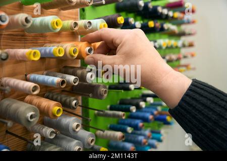 Man takes a spool of yellow thread from a rack Stock Photo