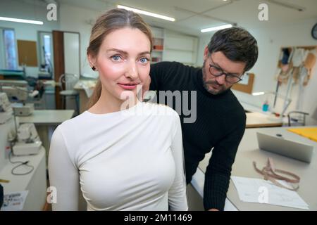 Male designer in a sewing studio takes measurements from woman Stock Photo
