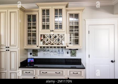 A cream colored new construction kitchen with black granite countertops clear glass cabinets and wine bottle storage Stock Photo