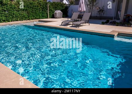 A rectangular new swimming pool with tan concrete edges in the fenced backyard of a new construction house Stock Photo