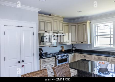 A cream colored new construction kitchen with black granite countertops and wood flooring and stainless steel appliances Stock Photo