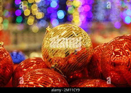 Christmas toys, golden and red balls on blurred festive lights background. New Year decorations in a store Stock Photo