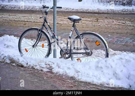 Riga, Latvia - 8 December, 2022: Bike chained to a pole on a city street in winter Stock Photo