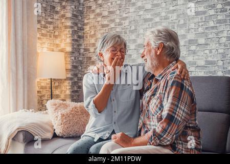 Couple of two seniors having fun together and enjoying on the sofa at home. Mature people talking and laughing hugged. Stock Photo