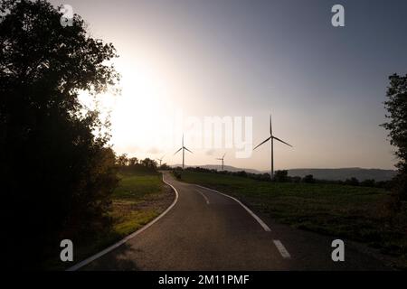 Road in agricultural fields with wind turbines generating clean electricity in Catalonia Spain Stock Photo