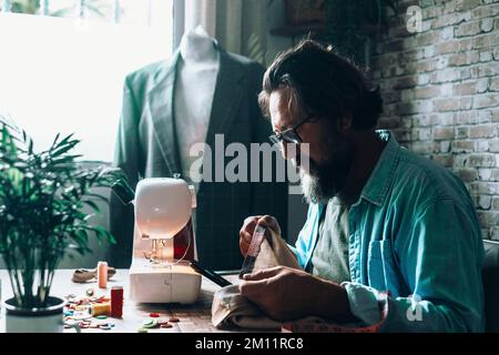 Man at home using sewing machine to tailor and modify garments. Blazer in background. Tailoring and tailor at work at the workshop. Concept of people and alternative job for woman. Professional tailor Stock Photo