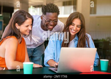 Group of happy friends students sitting in a cafe bar looking at laptop Stock Photo
