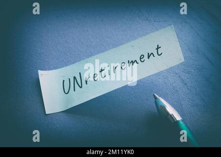 Unretirement word written on paper note with pen. Top view, flat lay on dark blue paper background. Stock Photo
