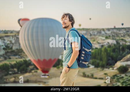 Tourist man looking at hot air balloons in Cappadocia, Turkey. Happy Travel in Turkey concept. Man on a mountain top enjoying wonderful view Stock Photo
