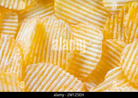 Yellow crispy ridged potato chips close up. Food background, banner, header, wallpaper. Stock Photo