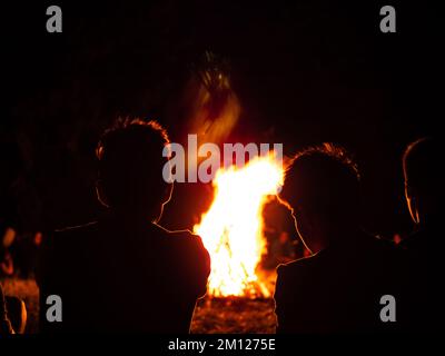 Young peoples' silhouette sitting around a campfire in a summer camp during night Stock Photo