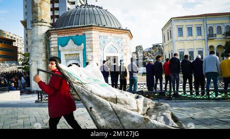 Muslims pray for Friday prayer in the garden of a historical Konak Mosque and people walk in front of this mosque in daily life of Izmir, Turkey. Stock Photo