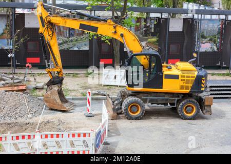 A large yellow wheeled excavator stands on the side of the road at a construction site in front of a fenced area on a summer day. Stock Photo