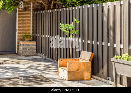 a small tree growing in a box on the sidewalk next to a wooden fence that has been painted with white paint Stock Photo