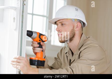 young contractor using cordless drill on door lock Stock Photo