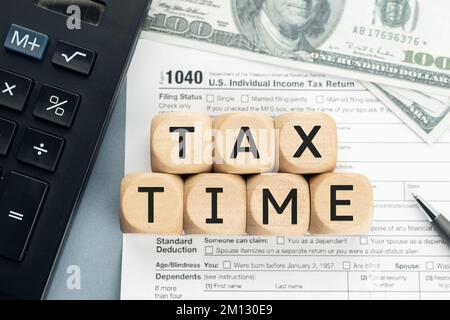 Tax Time concept. Wooden blocks with Tax time text, 1040 form, calculator and dollar banknotes Stock Photo