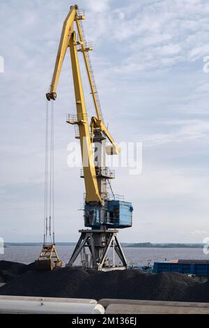 Rise tower crane over coastal terminal as charcoal is being loaded onto trains for transport  Stock Photo