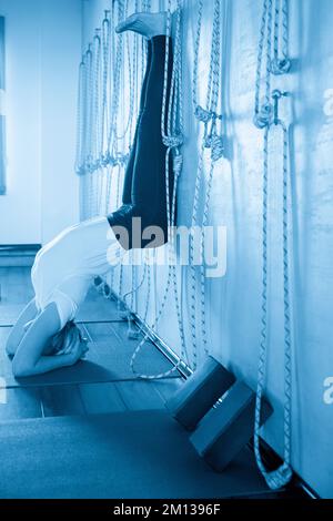 Young fit yogi woman practices yoga handstand near wall Stock Photo