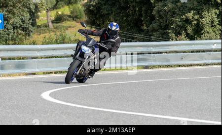 A male in a black outfit and blue helmet riding on a motorcycle in a  quiet street Stock Photo