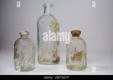 Two vintage glass vaccine bottles and one medical beaker, aged and patina on a white background. Empty and covered with dirt. Stock Photo