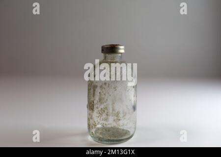 One dirty clear glass medical vaccine bottle, aged and patina on a white background.  Empty and covered with dirt and rust. Stock Photo