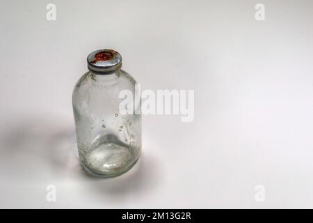 One dirty clear glass medical vaccine bottle, aged and patina on a white background.  Empty and covered with dirt and rust. Stock Photo