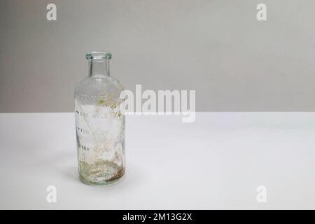 One dirty clear glass medical beaker, aged and patina on a white background.  Empty and covered with dirt and rust. Stock Photo