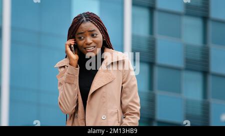 Young worried woman stands on street talking on phone upset because bad cellular connection worries about problem with mobile communication emotional Stock Photo