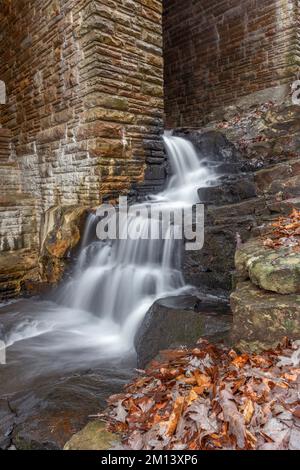 A small initial spillway on Byrd Creek Dam in Cumberland Mountain Tennessee shows the fall colors and brick details as the water flows down to the riv Stock Photo