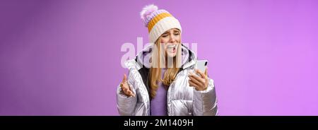 Bothered complaining dissatisfied cute blond girl yelling stupid smartphone standing unhappy recording audio message whining yelling mobile phone Stock Photo