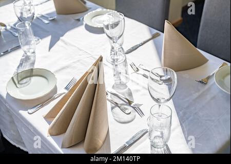 An empty dining table with glass cups, spoons, forks, knives and napkins with sunlight on it Stock Photo
