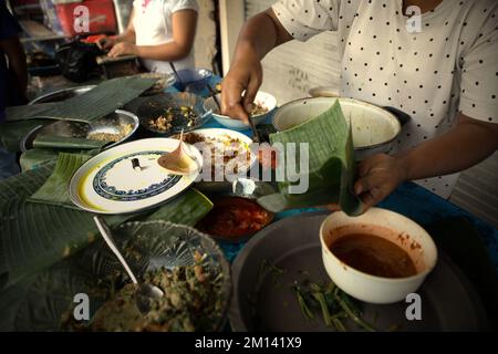 A woman serving customers at a street-side vendor offering food that was cooked traditionally in Klungkung, Bali, Indonesia. Stock Photo