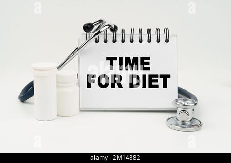 Medicine and health concept. On a white table lies a stethoscope, pills and a notebook with the inscription - TIME FOR DIET Stock Photo