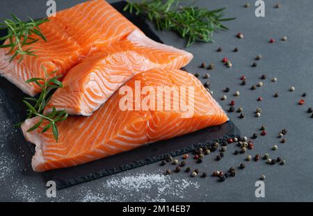Fresh salmon fillets on black cutting board with herbs and spice Stock Photo